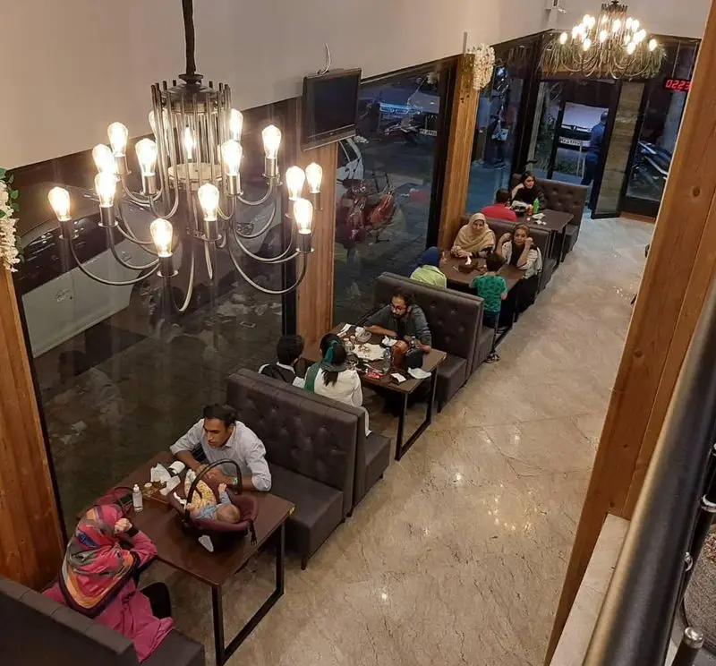 نمایی از فضای داخلی رستوران پیتزا دکتر آرین با دکوراسیون مدرن، لوسترهای چشمگیر و مشتریان شاد در حال لذت از غذایشان.