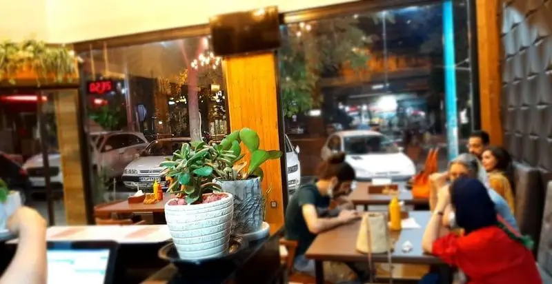 محیط داخلی دنج و دلنشین پیتزا دکتر آرین (اورجینال فود) در شب، با حضور مشتریان و نمای بیرونی خیابان شلوغ، مناسب برای صرف شام.