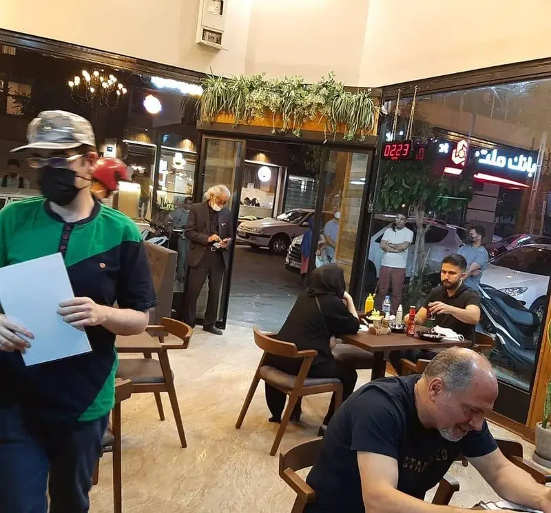 تصویری از محیط داخلی پیتزا دکتر آرین (اورجینال فود) در شب، با مشتریان نشسته و پرسنل، همراه با نمای خیابان شلوغ بیرون.