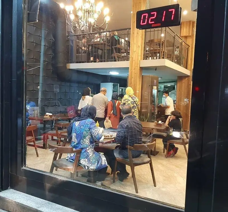 نمای داخلی پیتزا دکتر آرین (اورجینال فود) با مشتریان در حال صرف غذا، شامل فضای دنج و دو طبقه رستوران. محیطی عالی برای تجربه غذای خوشمزه.