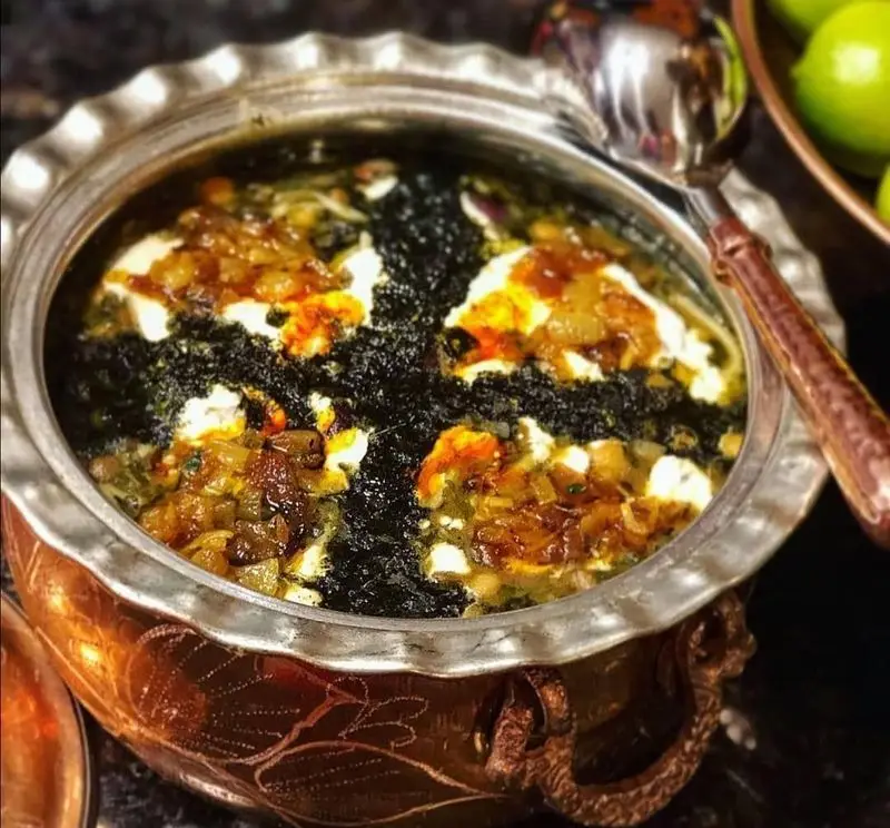 تصویر نمای نزدیک از آش خوش طعم و سنتی شیرازی در دیگ مسی قدیمی و زیبای رستوران آش مشتی شیرازی با تزئینات پیاز داغ و کشک.