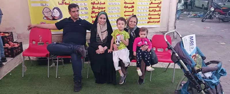 مشتریان ننه آقا شهرری، خانواده‌ای با کودکان در فضای بیرونی فروشگاه میوه، تجربه خرید دلنشین و محصولات با کیفیت.