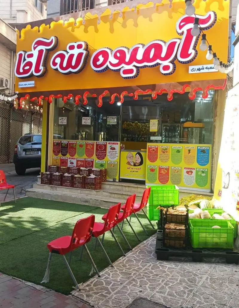 نمای بیرونی آبمیوه و میوه فروشی ننه آقا شعبه شهرری با صندلی‌های قرمز و میوه‌های تازه. بهترین آبمیوه در شهرری.