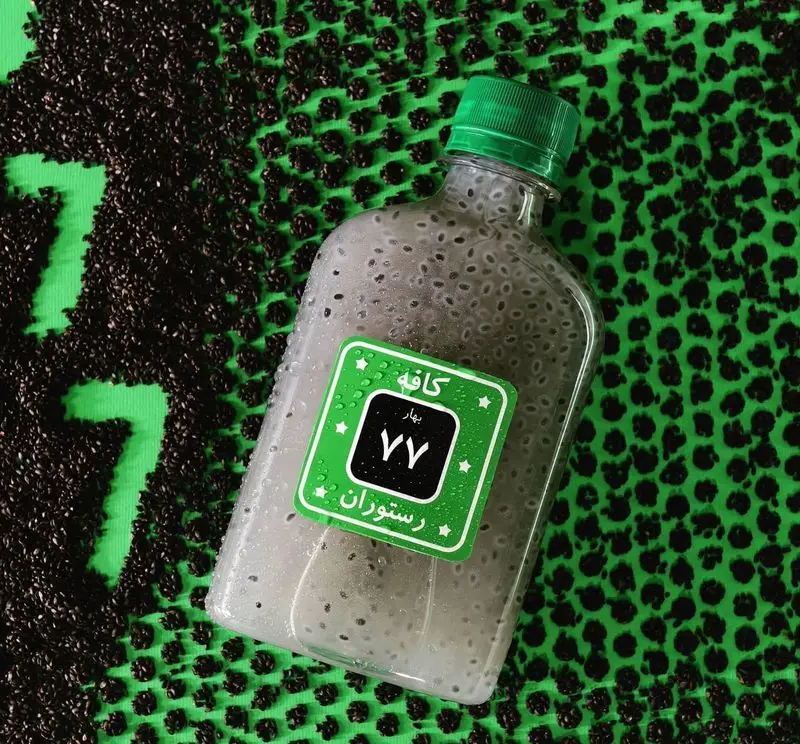 نوشیدنی خنک تخم شربتی یا چیا از کافه و رستوران ۷۷ در بطری شفاف با لیبل سبز و جذاب. پس‌زمینه سبز با الگوهای مشکی عدد ۷.