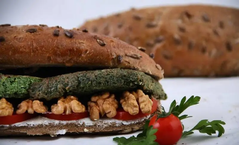 ساندویچ گیاهی رستوران و کافه ۷۷: نان سبوس‌دار با تخمه، پتی اسفناج، گوجه، گردو و پنیر خامه‌ای. غذایی سالم و انتخابی عالی برای شما.