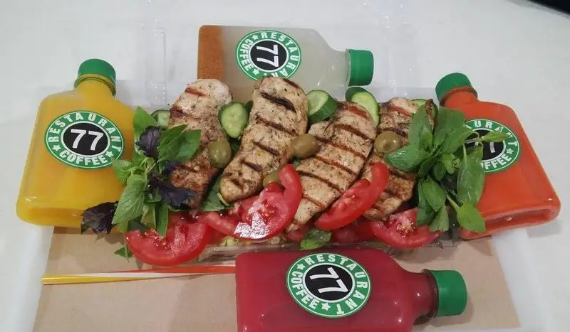 عکس از وعده غذایی سالم رستوران و کافه ۷۷: مرغ گریل، گوجه، خیار، زیتون و سبزیجات تازه با نوشیدنی‌های متنوع برند ۷۷.