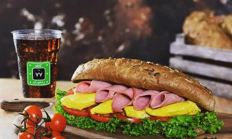 ساندویچ ژامبون و پنیر خوش‌طعم و تازه کافه و رستوران ۷۷ با نان سبوس‌دار، همراه با نوشیدنی خنک و گوجه فرنگی گیلاسی.