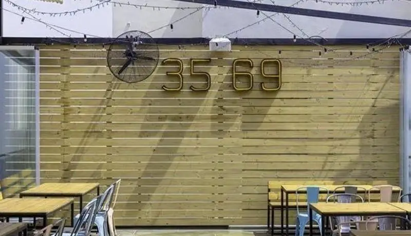 فضای باز دلنشین و دنج جو گریل فود با دیوار چوبی، میز و صندلی مدرن و ریسه‌های نوری، انتخابی عالی برای صرف غذاهای لذیذ گریل.