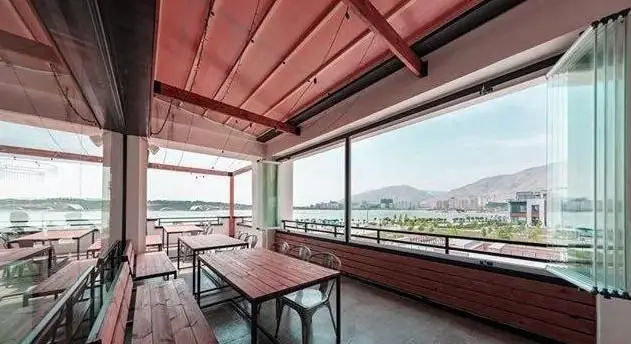 رستوران جو گریل فود، فضای بالکن با طراحی چوبی و سقف جمع‌شونده، مناسب صرف غذا با منظره دریا و شهر