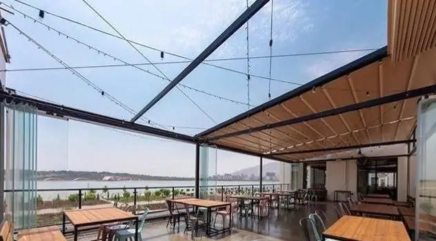 فضای روف گاردن دلنشین رستوران جو گریل فود با سقف متحرک، میز و صندلی چوبی و چشم‌انداز زیبا به دریاچه، محیطی ایده‌آل برای صرف غذا.