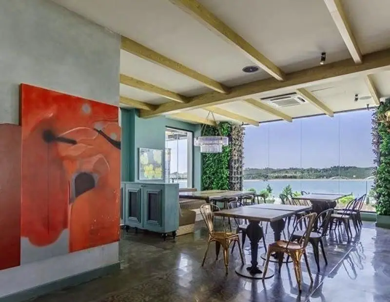 رستوران جو گریل فود: فضای داخلی مدرن با منظره چشم‌نواز دریاچه، میز و صندلی‌های شیک، تابلوی هنری و دیوارهای سبز خاص.