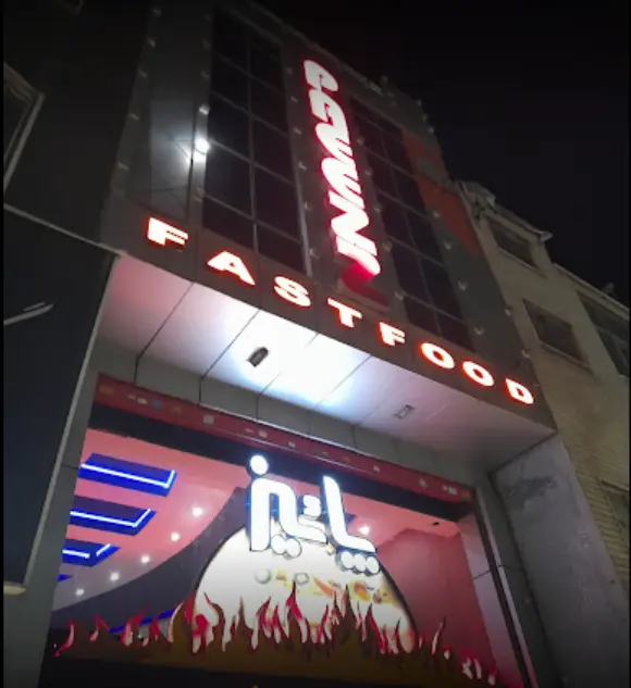 تصویر نمای بیرونی شبانه فست فود پاییز نازی آباد، با تابلوهای روشن "FASTFOOD" و "پاییز" و طراحی آتشین جذاب.