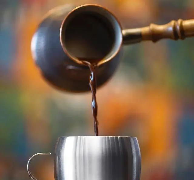 ریختن قهوه تازه دم شده از قهوه‌جوش سنتی به فنجان نقره‌ای، تصویری دلنشین از کیفیت نوشیدنی‌های فست فود ب ب ک برای تجربه‌ای متفاوت.