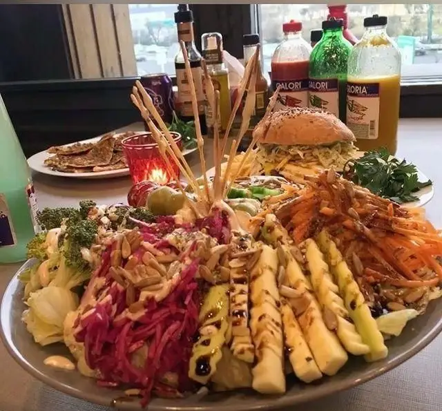 بشقاب بزرگ و متنوع فست فود ب ب ک شامل انواع سالاد تازه (بروکلی، کلم، هویج)، برگر، سبزیجات و سس‌های رژیمی در محیط رستوران.