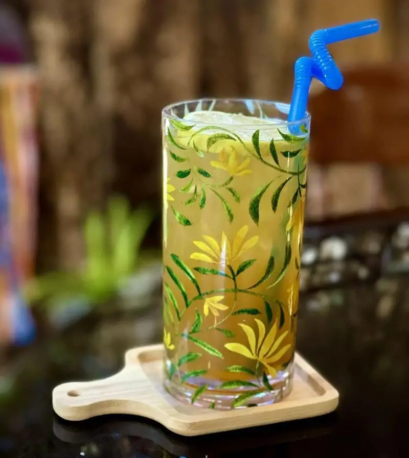 نوشیدنی خنک و گوارای کافه دلواز با طرح گل و برگ‌های زیبا روی لیوان خاص، به همراه نی آبی. لحظات دلنشین تابستان را در کافه دلواز تجربه کنید.