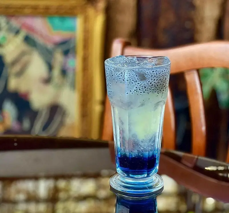 نوشیدنی خنک و خوشرنگ تخم شربتی کافه دلواز، لایه‌بندی آبی و روشن، همراه با یخ، در محیطی آرام و هنری. تجربه‌ای دلنشین.