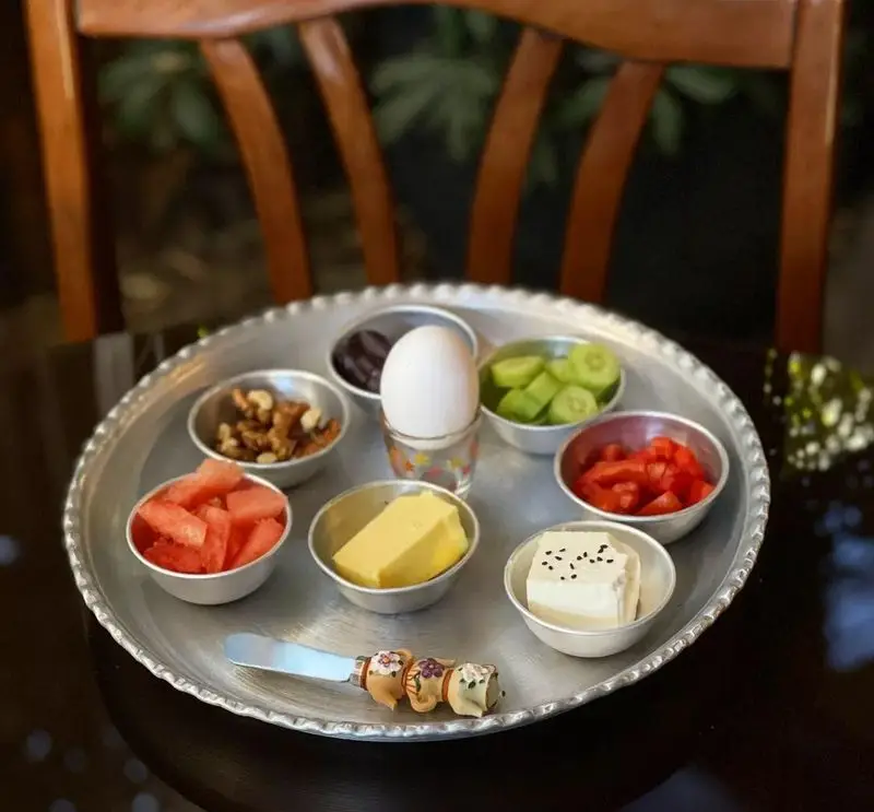 سینی صبحانه متنوع و خوشمزه کافه دلواز شامل تخم مرغ، پنیر، کره، هندوانه، گردو، خیار و گوجه فرنگی تازه برای شروع روز.