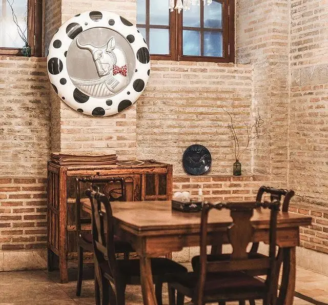 فضای داخلی دنج روحی اکسپرس تجریش: دیوار آجری، میز و صندلی چوبی، آینه دکوراتیو با طرح گاو و پاپیون، محیطی دلنشین برای کافه و رستوران.