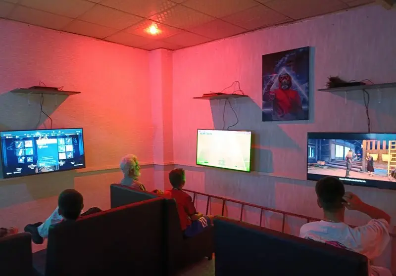 تصویری از پاتوق کافه گیم شو و گیم نت: جوانان و گیمرها در حال تجربه بازی‌های ویدیویی پرطرفدار روی تلویزیون‌های بزرگ در فضایی جذاب.