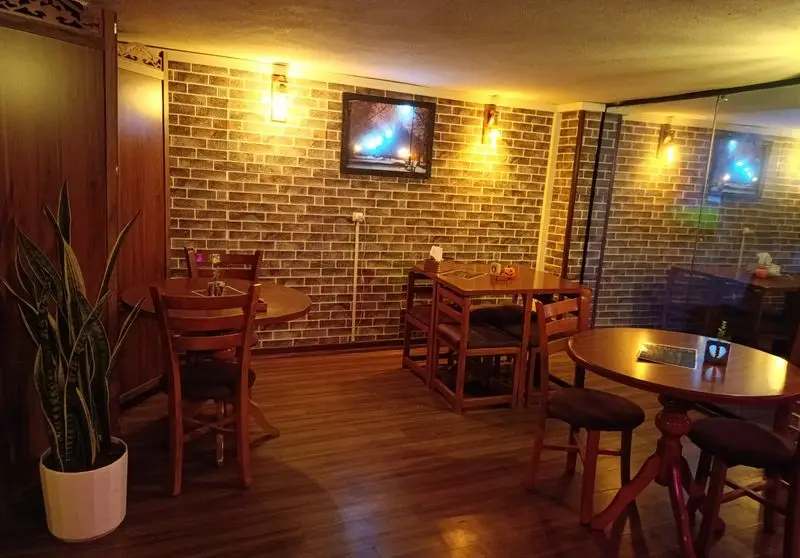 فضای داخلی دنج کافه گیم شو و کافه کتاب مافیا گیم نت با میز و صندلی چوبی، دیوار آجری و نورپردازی گرم