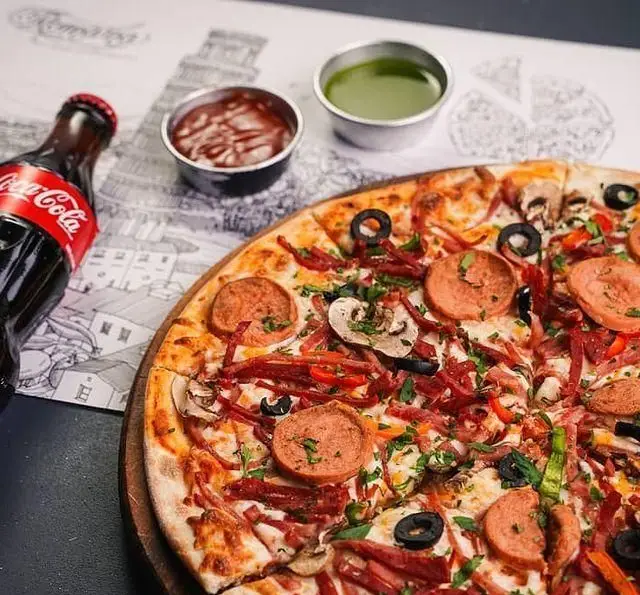 پیتزای عالی و پرطرفدار "رستوران ایتالیایی رومانا" با تاپینگ‌های متنوع سوسیس، بیکن، قارچ، زیتون و سبزیجات تازه، همراه با نوشابه.