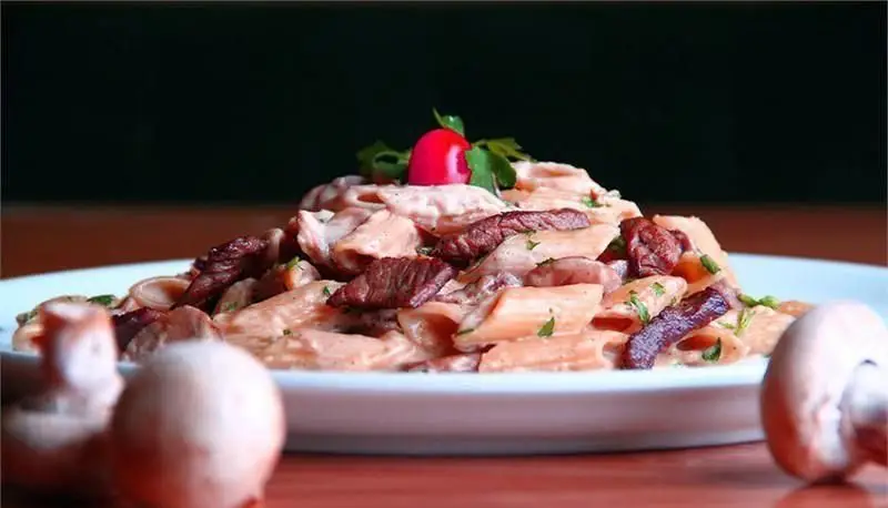 پاستا پنه با تکه های گوشت آبدار و قارچ، همراه با سس خامه ای صورتی، تزئین شده با گوجه فرنگی کوچک. از رستوران ایتالیایی رومانا.