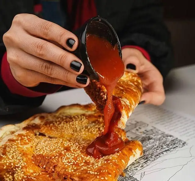 ریختن سس کچاپ روی نان تازه کنجدی در رستوران ایتالیایی رومانا. تجربه‌ای لذت‌بخش از غذاهای ایتالیایی داغ و خوشمزه.