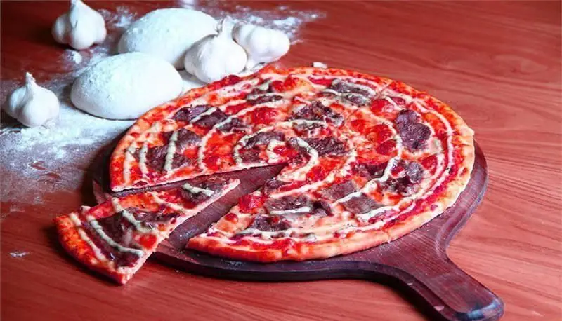 پیتزا گوشت تازه و خوشمزه رومانا روی تخته سرو چوبی با خمیر پیتزای دست‌ساز و سیر در پس‌زمینه. غذای اصیل ایتالیایی در رستوران رومانا.