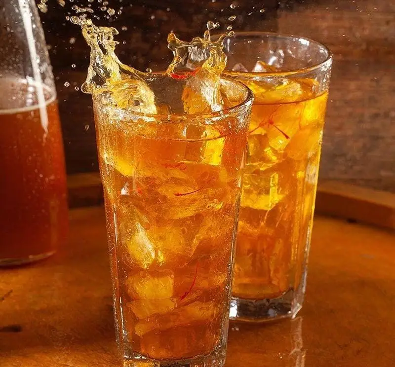 نوشیدنی خنک زعفرانی با تکه‌های یخ و پاشش دلچسب مایع در لیوانی بلند، ایده‌آل برای رفع عطش. تجربه‌ای گوارا و تازه در فست فود باگت.