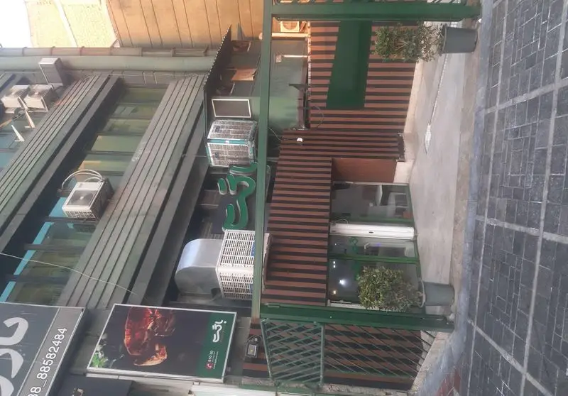 نمای خارجی فست فود باگت در خیابان، شامل تابلوی سبز رنگ با نام باگت، دکوراسیون چوبی و شیشه‌ای ورودی و تبلیغ غذا.