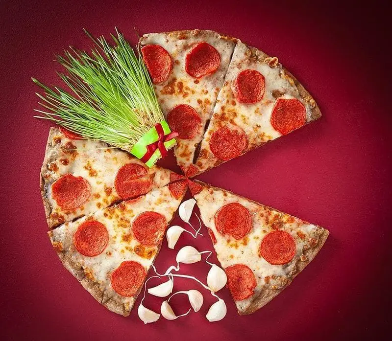 پیتزا پپرونی کامل با برش‌های مرتب، تزئین شده با سبزه تازه و حبه‌های سیر سفید، نمادی از کیفیت و طعم‌های دلپذیر در فست فود باگت.