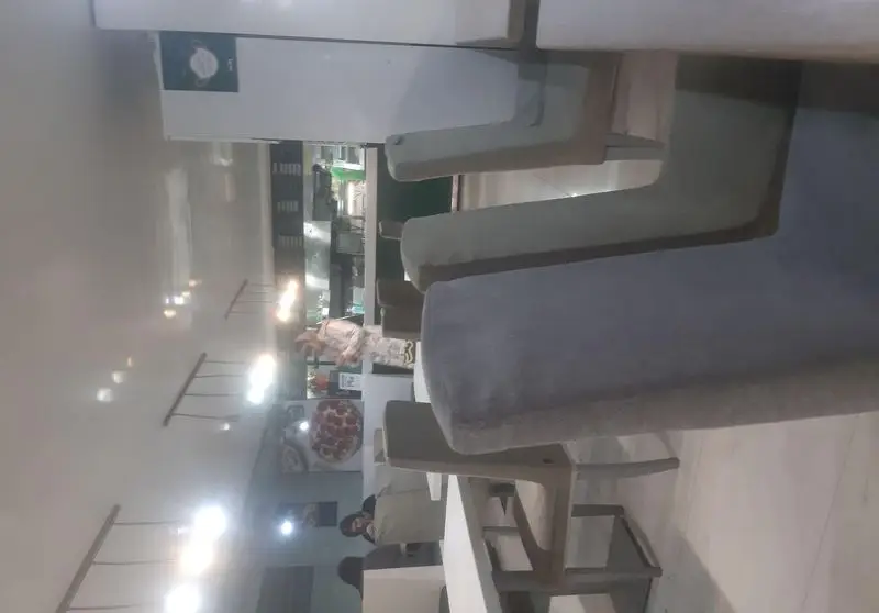 تصویری از دکوراسیون داخلی فست فود باگت شامل میزهای بلند و صندلی‌های مدرن، فضای غذاخوری تمیز و روشن، با آشپزخانه و مشتریان در پس‌زمینه.