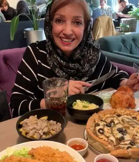 خانمی شاد و خندان در حال لذت بردن از غذای خوشمزه فست فود باگت شامل پیتزا و انواع پیش غذاها در یک محیط دلنشین رستوران.