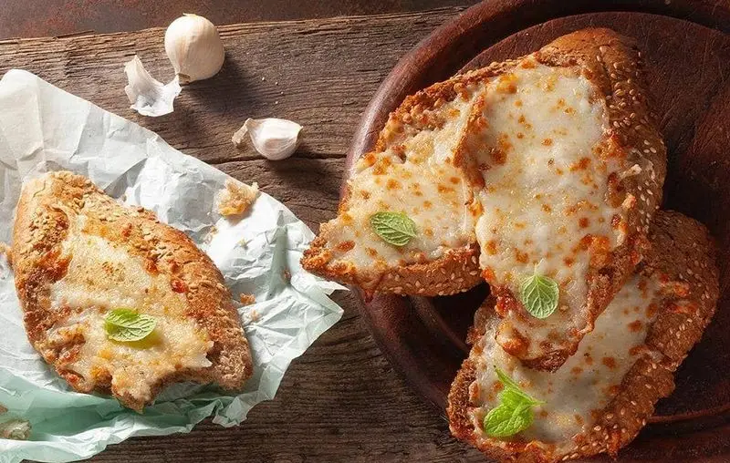 نان سیر و پنیر خوشمزه باگت؛ تکه‌های نان باگت برشته با پنیر آب شده، سیر و نعنا روی میز چوبی، مناسب فست فود باگت.