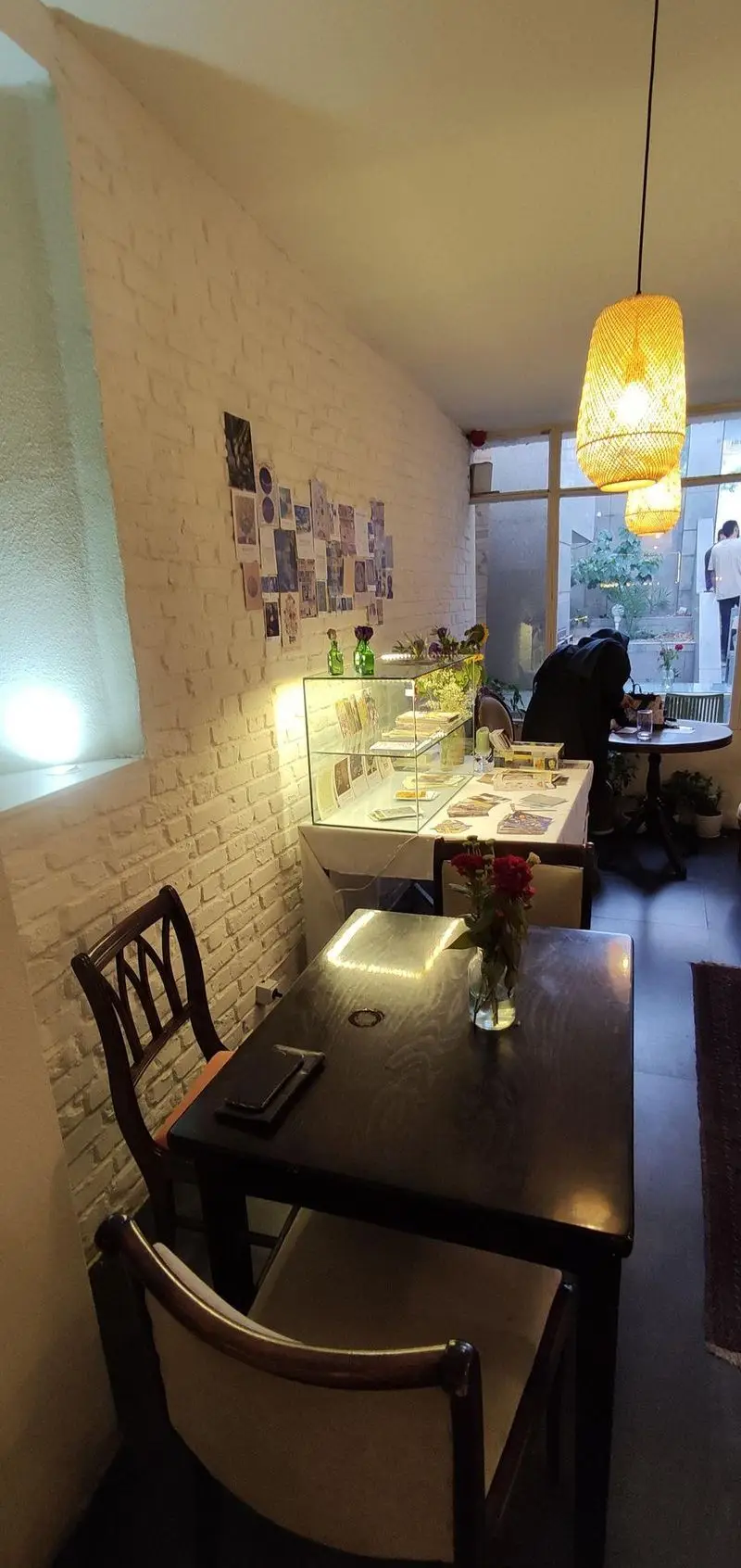 فضای داخلی دنج کافه الوا با دیوار آجری سفید، میز و صندلی چوبی شیک، ویترین نمایش محصولات و نورپردازی گرم، مناسب دورهمی.