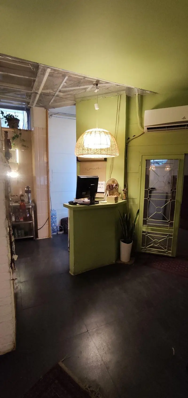 فضای داخلی کافه الوا: پیشخوان سبز، چراغ آویز حصیری، دیوارهای لیمویی و کف تیره. دکوراسیونی دلنشین و آرامش‌بخش برای مشتریان.