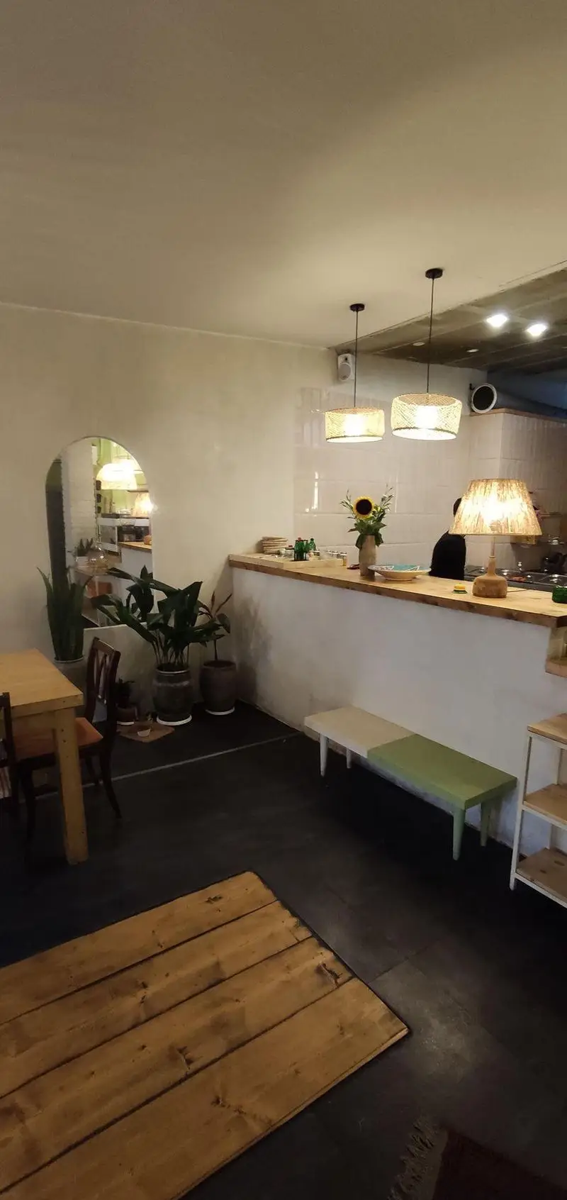 فضای داخلی کافه الوا با دکوراسیون دنج و مدرن شامل میز و صندلی چوبی، پیشخوان، گلدان و نورپردازی زیبا برای تجربه ای دلنشین.