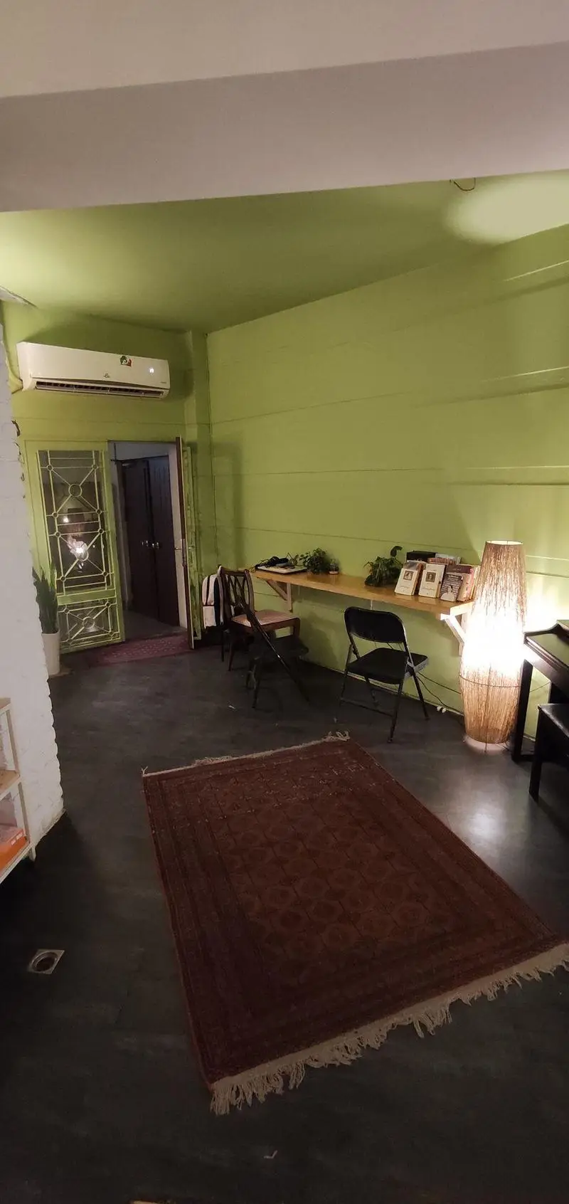 دکوراسیون داخلی کافه الوا: فضایی دنج و سرسبز با میز مطالعه چوبی، کتاب‌ها، نورپردازی گرم، فرش شرقی و صندلی‌های راحت.