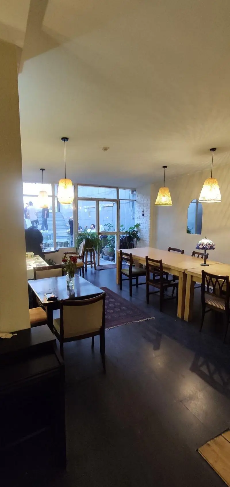 فضای داخلی کافه الوا با دکوراسیون گرم و صمیمی، میز و صندلی‌های چوبی، نورپردازی دلنشین و چشم‌انداز به فضای سبز بیرونی.