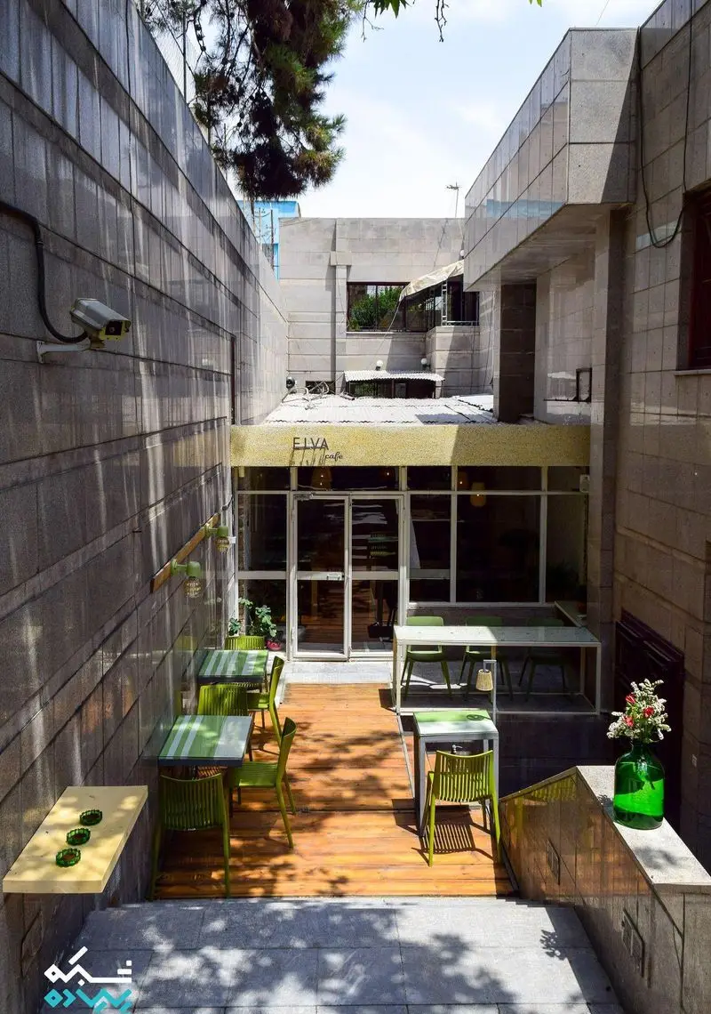 نمایی از فضای باز دنج و زیبای کافه الوا با میز و صندلی‌های مدرن سبز، طراحی خاص با دکوراسیون چوبی و سنگی، مناسب دورهمی.