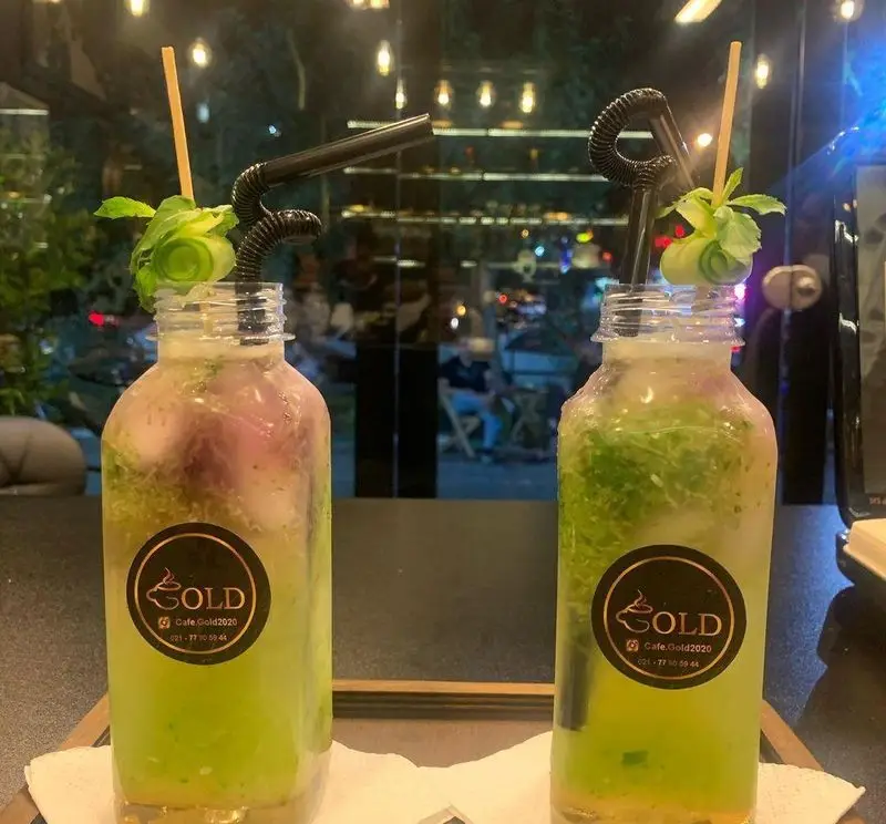 تصویری زیبا از دو نوشیدنی خنک و سبز کافه گلد، سرو شده در بطری‌های شیک، تزئین شده با برگ نعنا و خیار، مناسب برای تجربه دلپذیر در کافه.