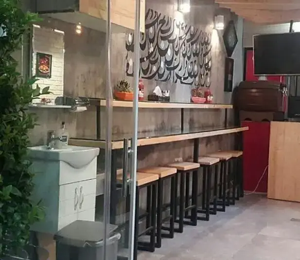 فضای داخلی دلنشین و دکوراسیون مدرن فست فود سرزمین لقمه شامل میز و صندلی‌های بار، دیوار کالیگرافی و سینک بهداشتی برای راحتی مشتریان.