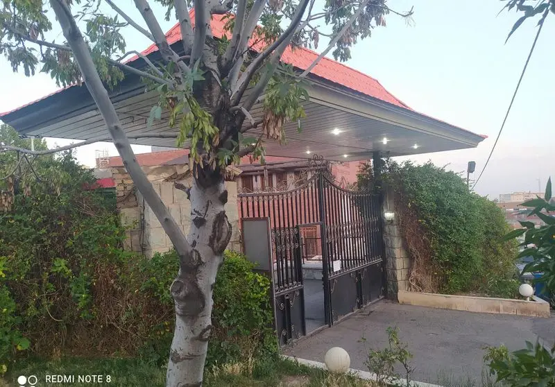 این تصویر ورودی اصلی و دلنشین رستوران بوستان ناجا را با دروازه فلزی بزرگ، سقف سایبان و درختان سرسبز باغ نشان می‌دهد.