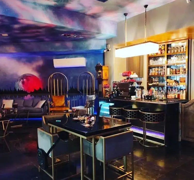 دکوراسیون داخلی منحصر به فرد کافه شیرز: فضای شیک با بار مجهز، میزهای مدرن، صندلی‌های فانتزی و نقاشی دیواری رؤیایی با نورپردازی خاص.