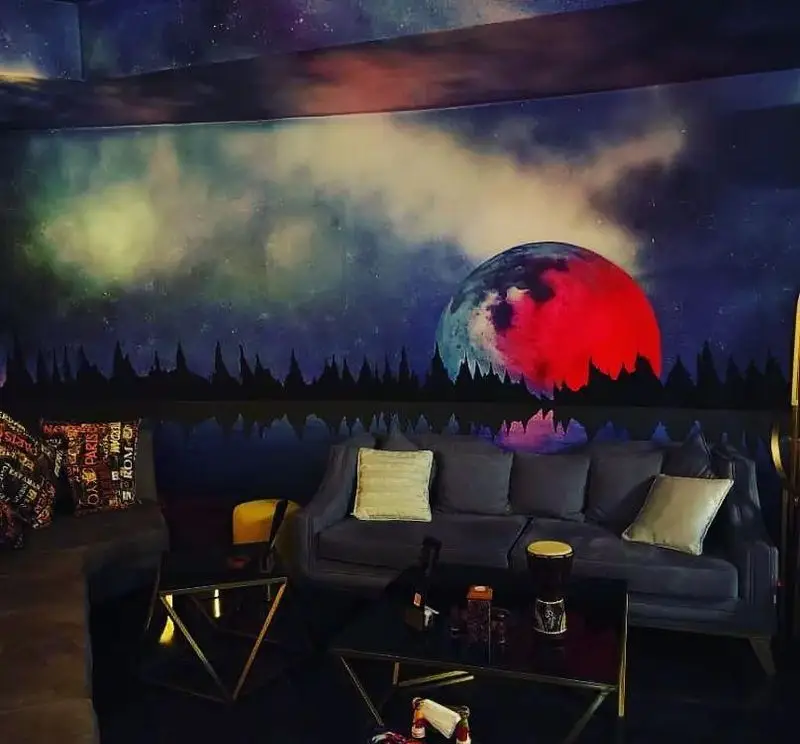 فضای داخلی کافه شیرز با دکوراسیون منحصر به فرد شامل دیوارنگاری زیبای آسمان پرستاره، ماه و جنگل، مبلمان راحت برای تجربه ای خاص.