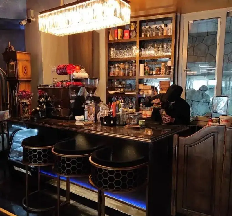 دکوراسیون داخلی کافه شیرز (ShieRez cafe) با میز بار لوکس، صندلی‌های شیک و قفسه‌های پر از نوشیدنی، محیطی دلنشین برای مشتریان.