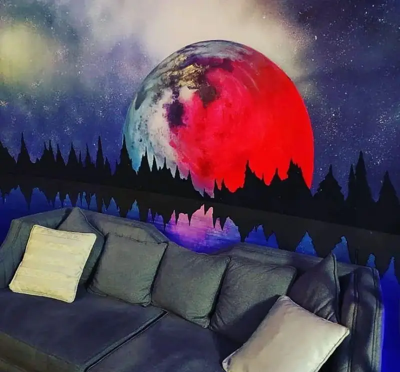 نمای داخلی کافه شیرز با طراحی دکوراسیون منحصربفرد، شامل دیوارنگاره ماه سرخ و آبی در فضای کهکشانی و مبلمان راحت کافه.