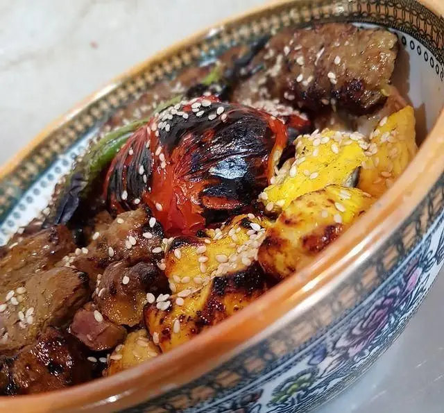 تصویری جذاب از کباب و جوجه کباب لذیذ کترینگ شاهین، همراه با گوجه و فلفل کبابی و کنجد. بهترین غذای ایرانی برای سفارش شما.