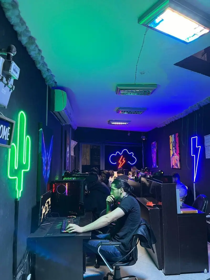 گیم نت بلک پلتفرم: محیطی پویا با نورپردازی نئون، از جمله کاکتوس سبز و رعد آبی، و بازیکنانی در حال تجربه بازی‌های کامپیوتری در فضایی تاریک و مدرن.