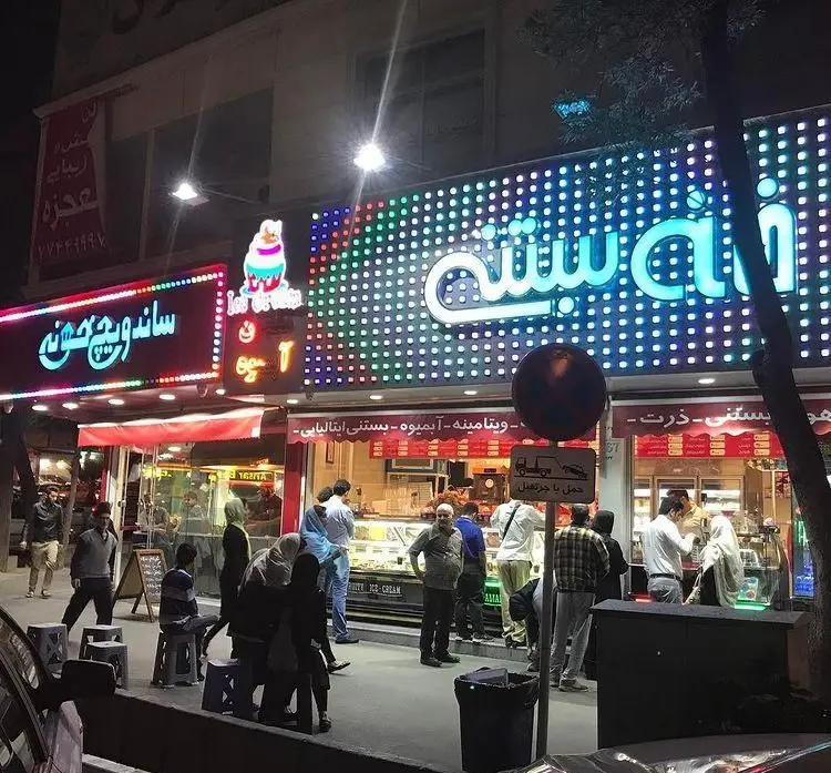 "ساندویچ خونه" یک فست فود محبوب در شب با تابلوهای نورانی، در کنار آبمیوه و بستنی فروشی، میزبان مشتریان پرشمار در خیابان شهر.